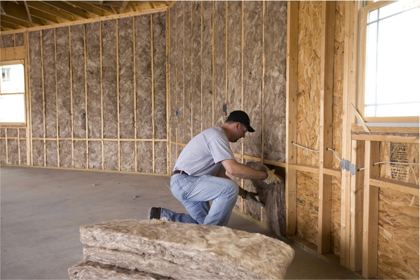 Brazos Thermal worker installing fiberglass batt insulation by hand wearing gloves.