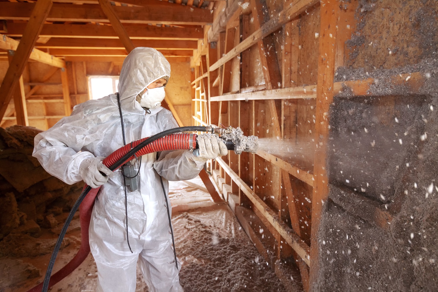 Brazos thermal worker in protective gear using tools to spray cellulose insulation.