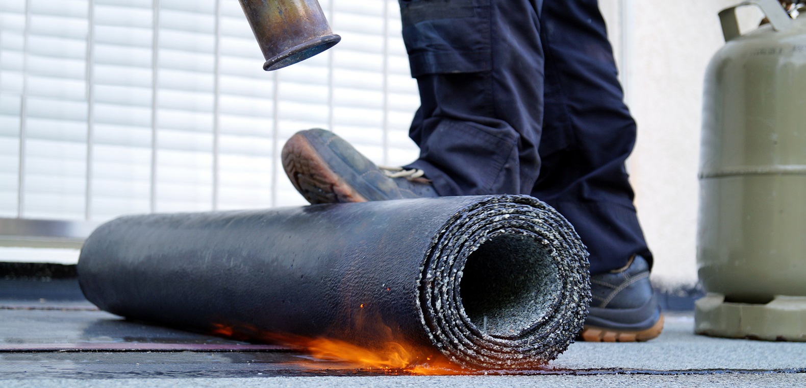 Brazos Thermal worker in uniform and safety gear working on installing modified bitumen roofing.