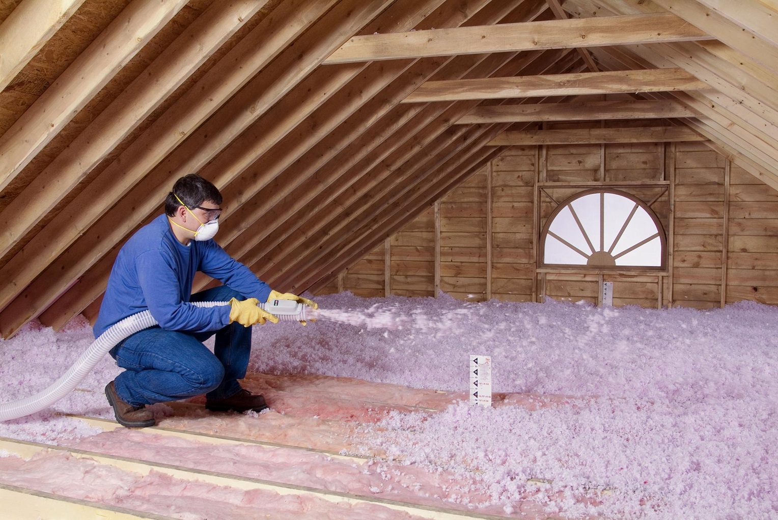 Brazos Thermal worker spraying blown-in fiberglass insulation with protective gear on.