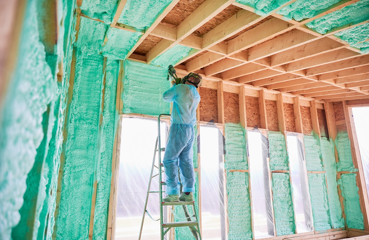 Brazos Thermal worker on a ladder using a tool to spray closed cell foam insulation.