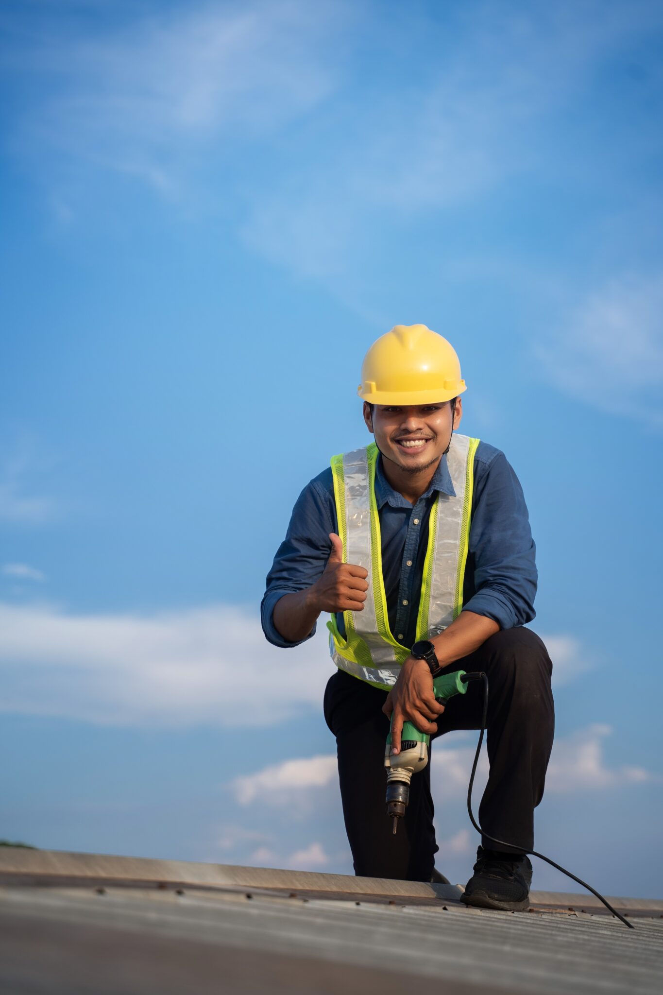 Worker in safety gear holding a tool up with one thumb up smiling.