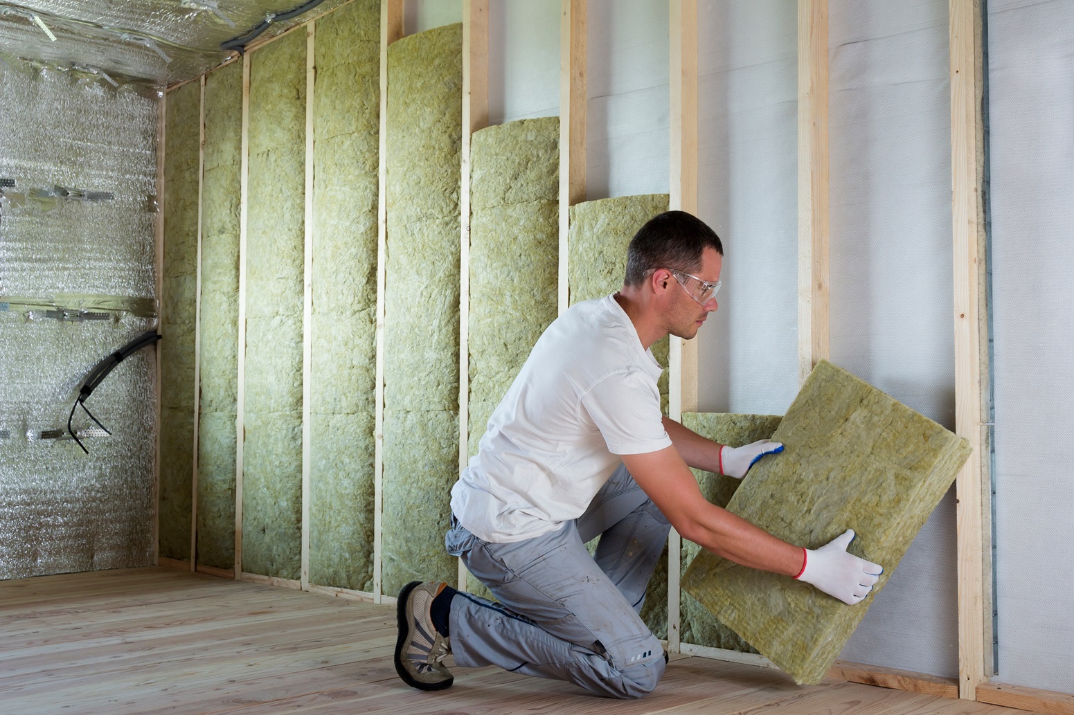 Brazos Thermal worker installing sound proofed insulation in home by hand with gloves on.