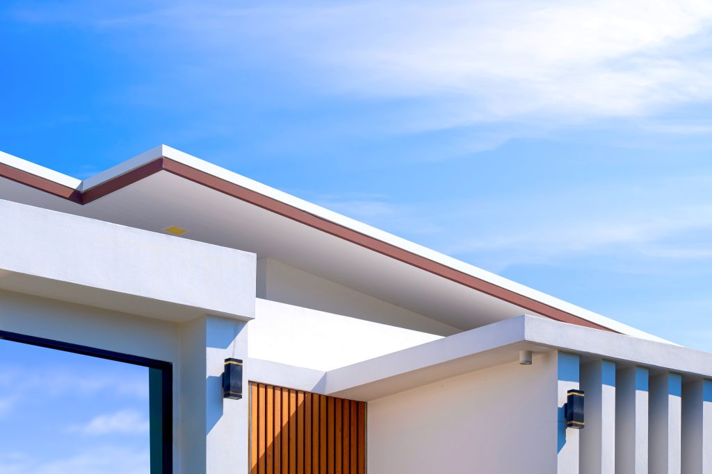 The top of a white building with a blue, partly cloudy sky behind it.