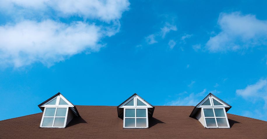A roof with three windows against a blue sky.