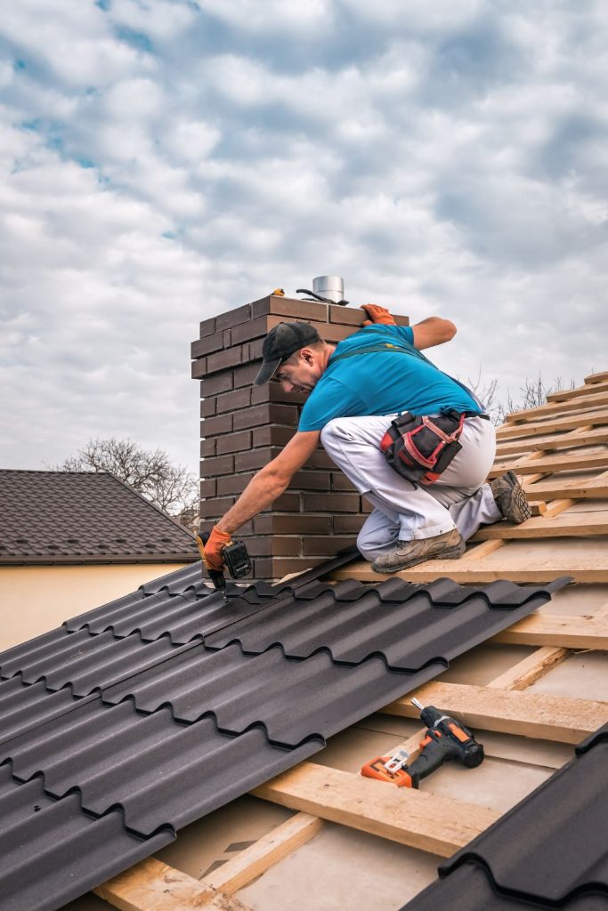 A man in a blue shirt uses a drill to secure roof tiles on a cloudy day.