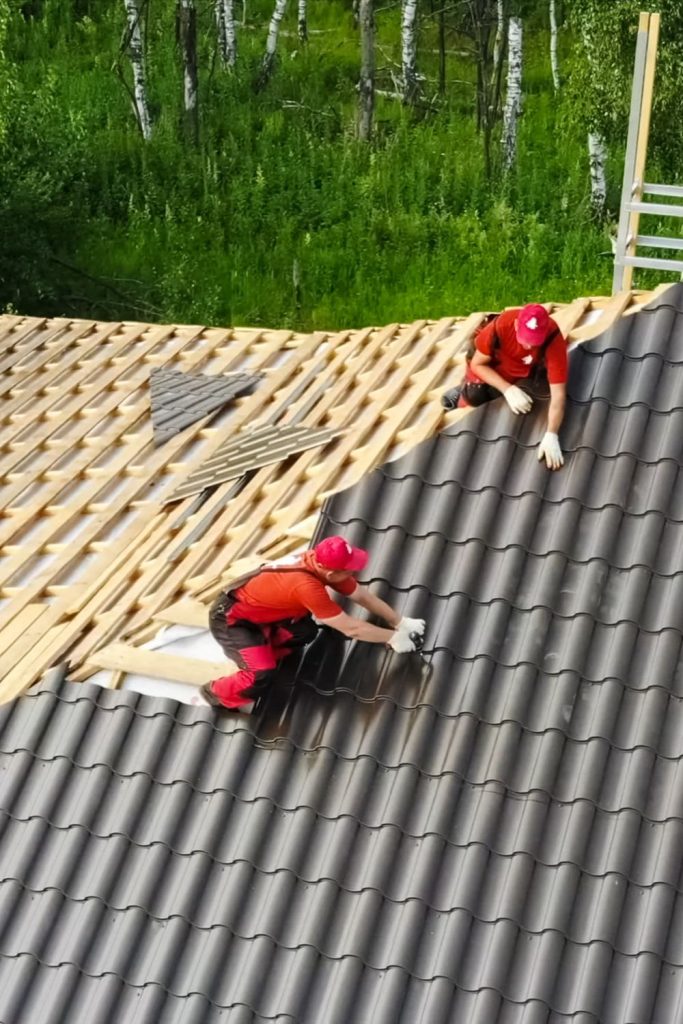 Two people in red shirts and overalls work on a roof.