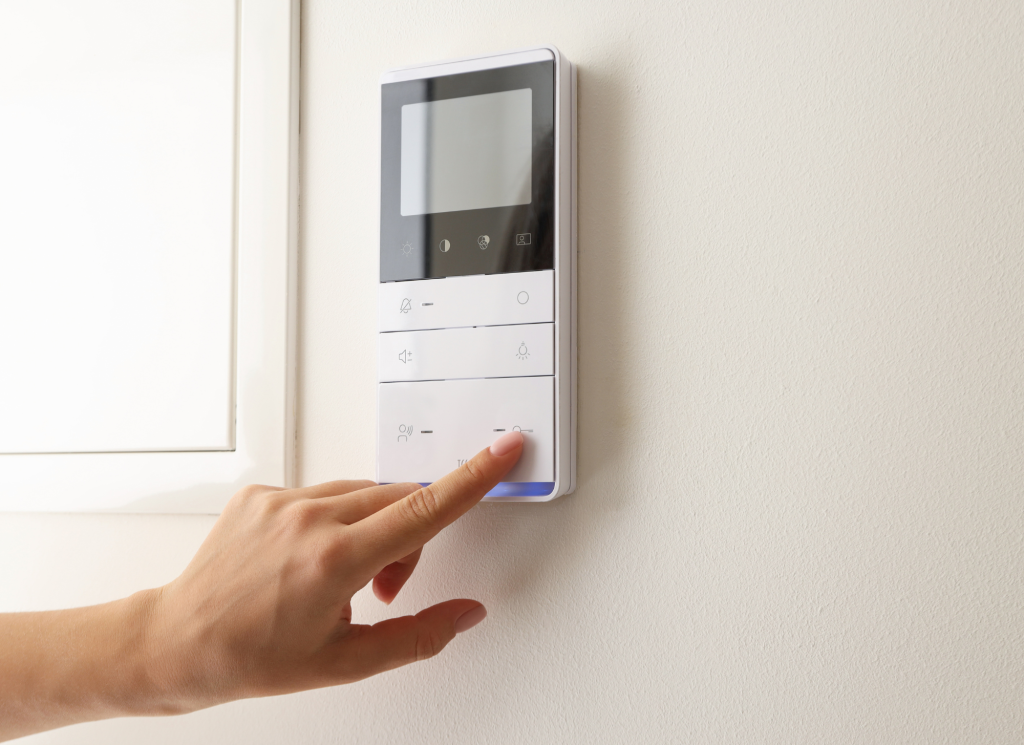 A hand presses buttons on a digital thermostat hanging on a white wall.