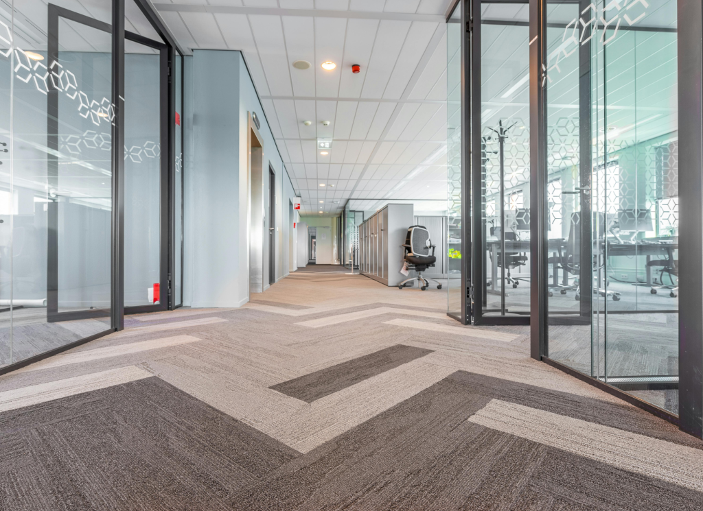 An office with patterned, beige carpet and glass walls.