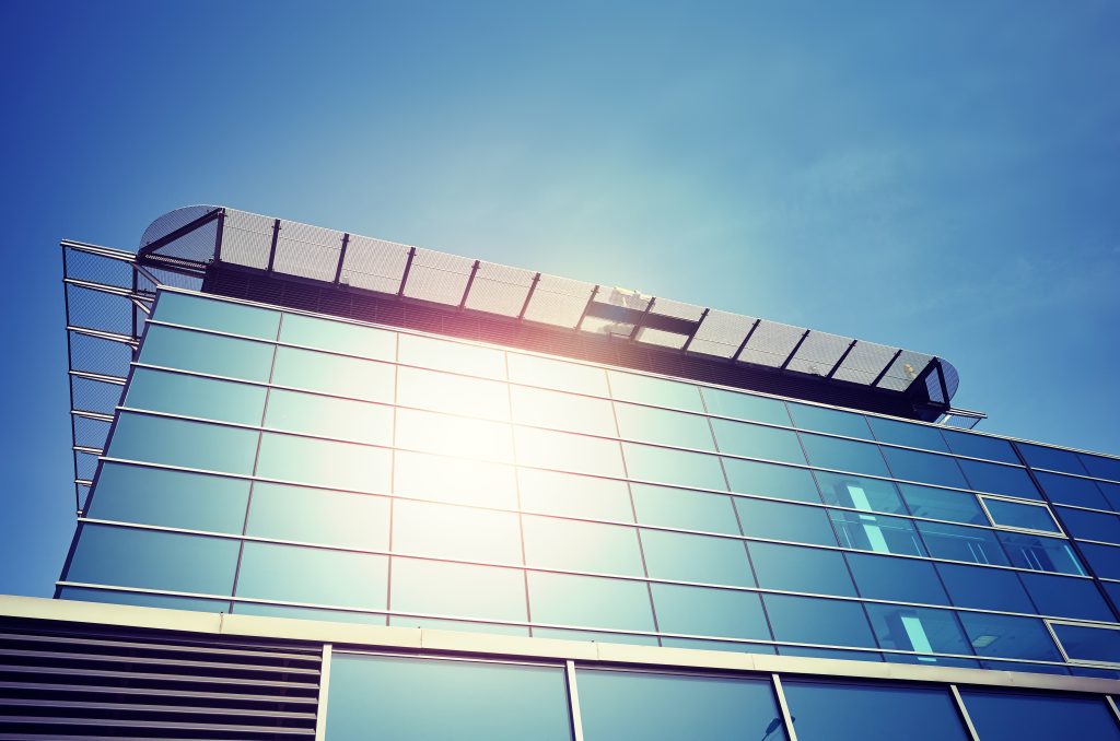 A low-angle view of a modern building. The sun reflects off of its windows.