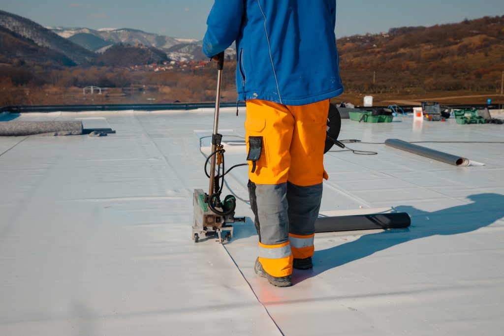 A person wearing a blue coat and orange high-visibility pants works on a flat roof.