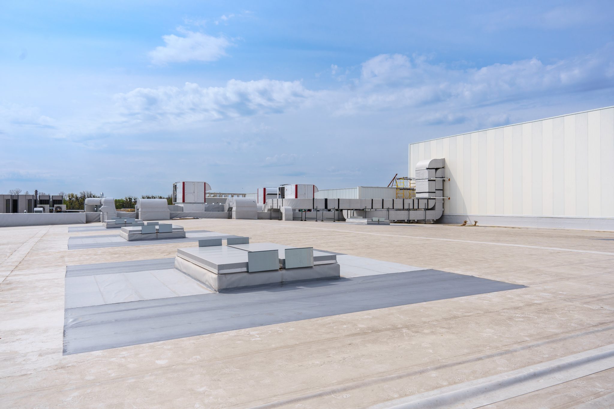 A flat roof with an HVAC system on a partly cloudy day.