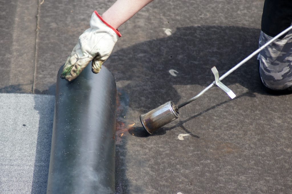 A close-up of a person using a blow torch on a roof.
