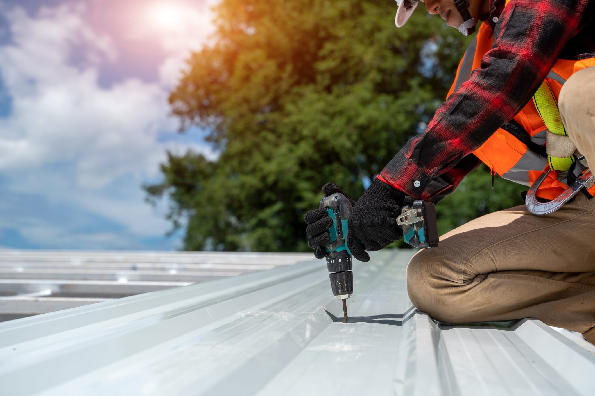 A person wearing a red and black flannel uses a drill on a white roof.