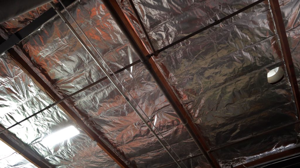 A radiant barrier covers insulation on the ceiling of a warehouse.