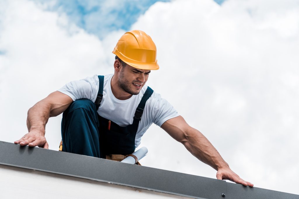 A man in a yellow hard hat inspects a roof.