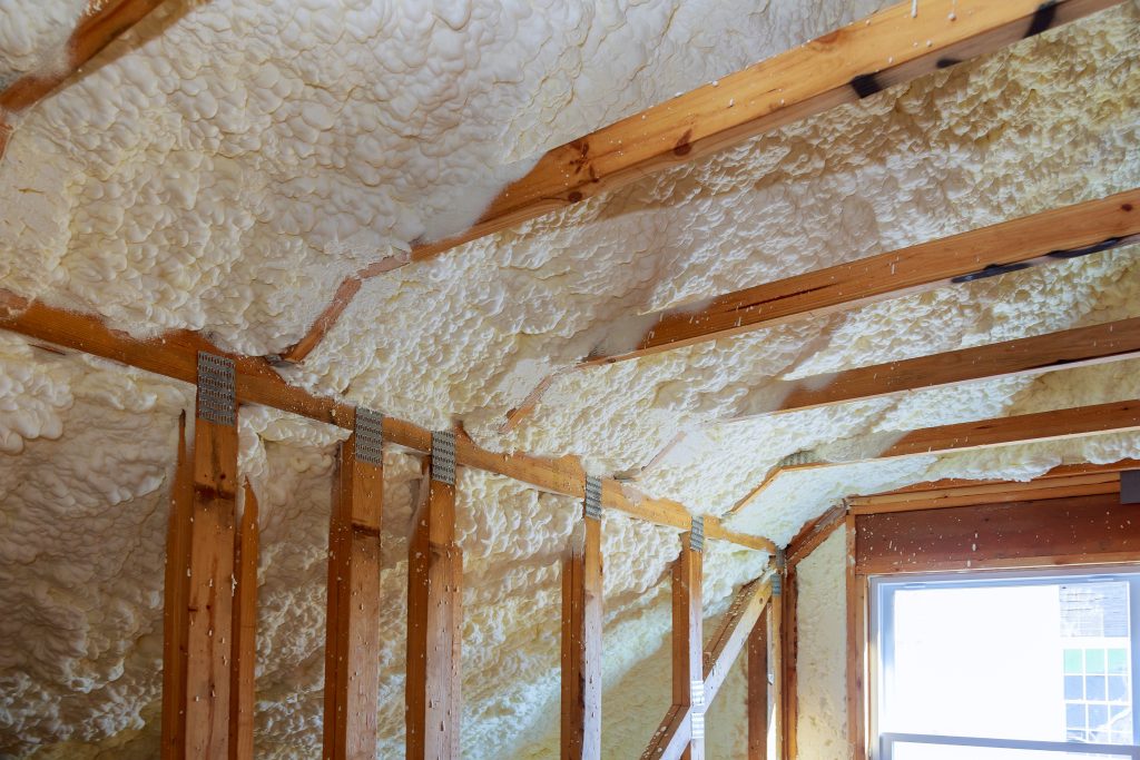 White spray foam insulation covers the ceiling and wall of a building.