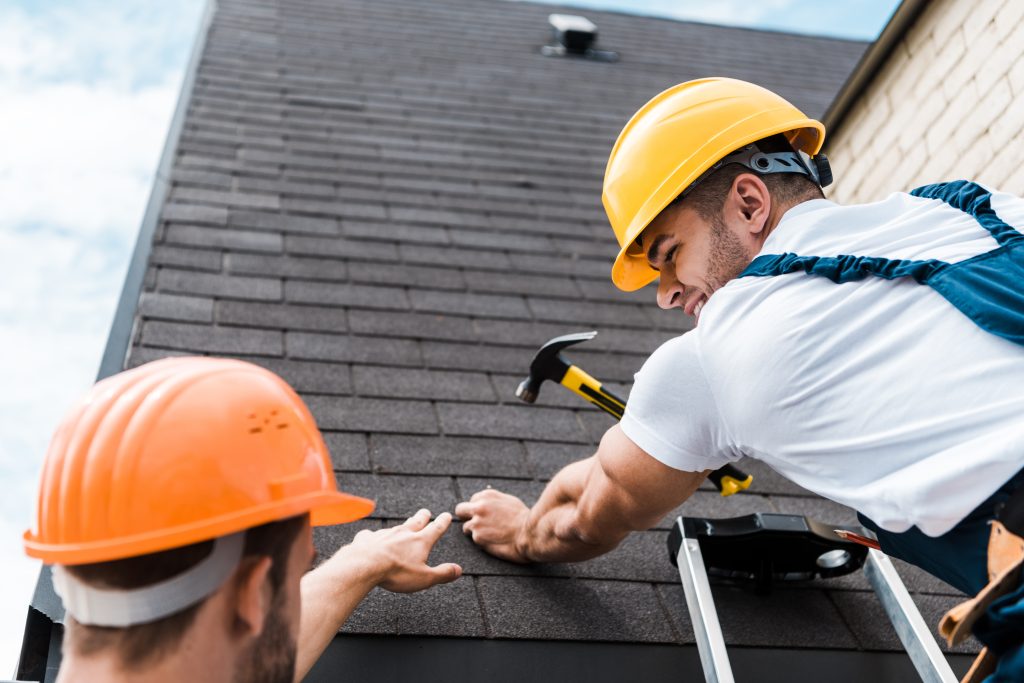 Two men in hard hats work on a roof.